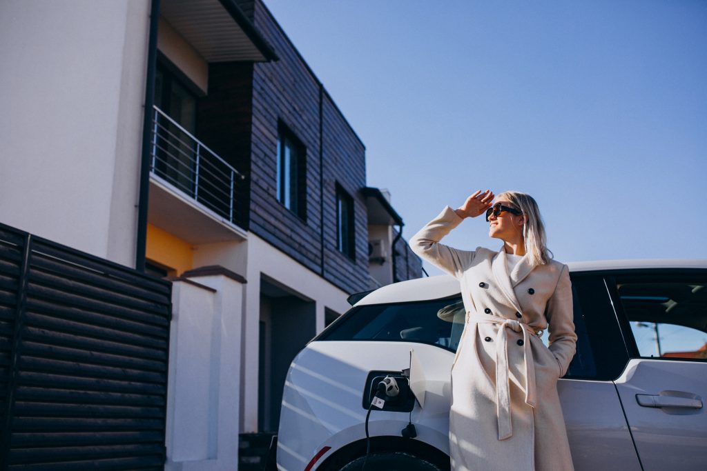 Mujer junto a una vivienda moderna y un vehículo eléctrico