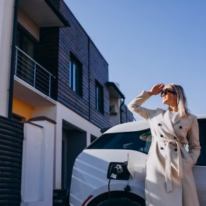 Mujer junto a una vivienda moderna y un vehículo eléctrico